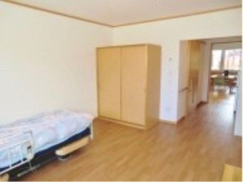 居室の床はフローリングになっており、ベッド、収納家具が設置されている。壁と天井の色は白色基調になっている。