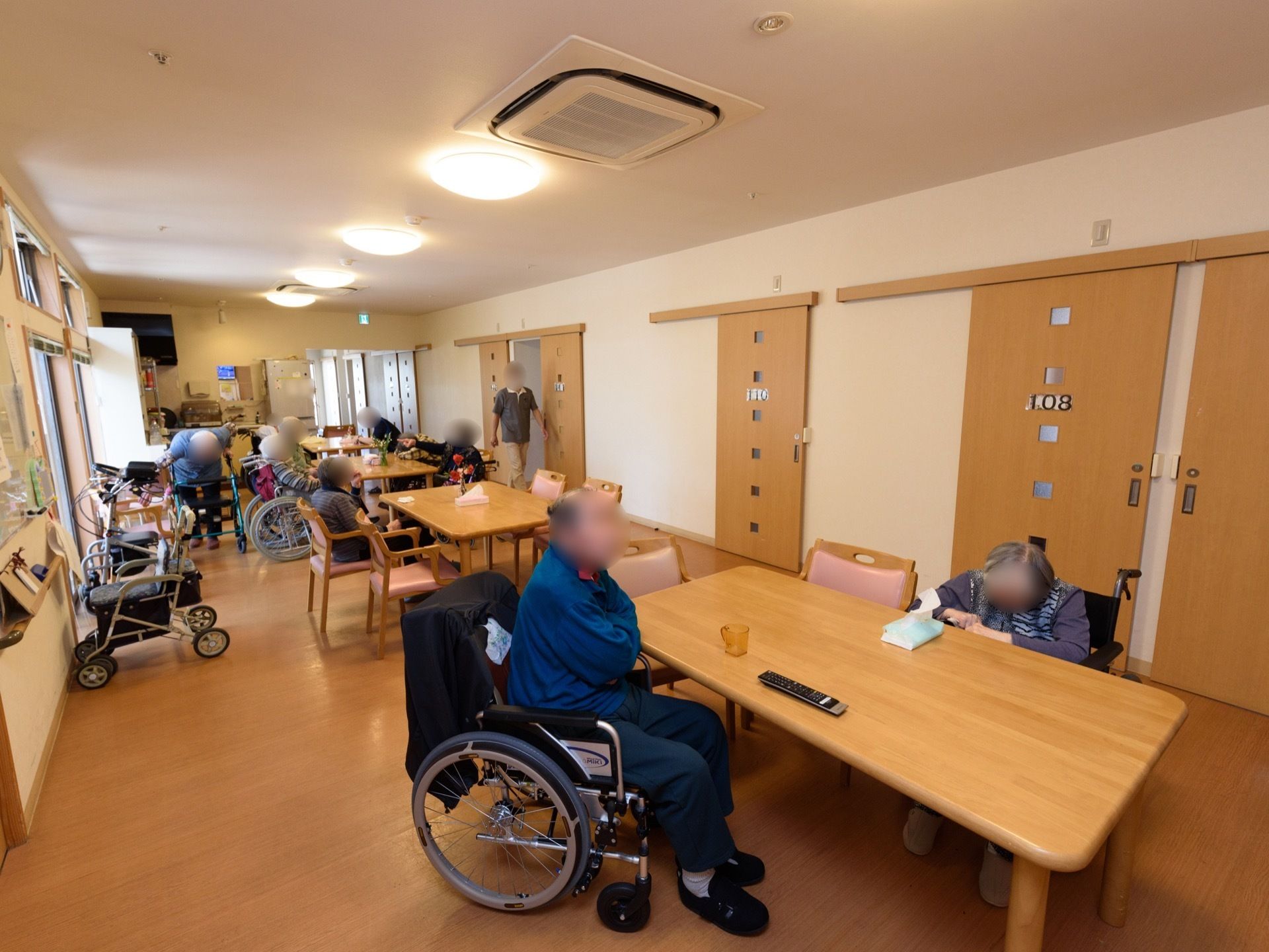 ダイニングテーブルが並んでおり、たくさんの入居者様が集っている。車椅子に乗ったまま席についている方もいる。