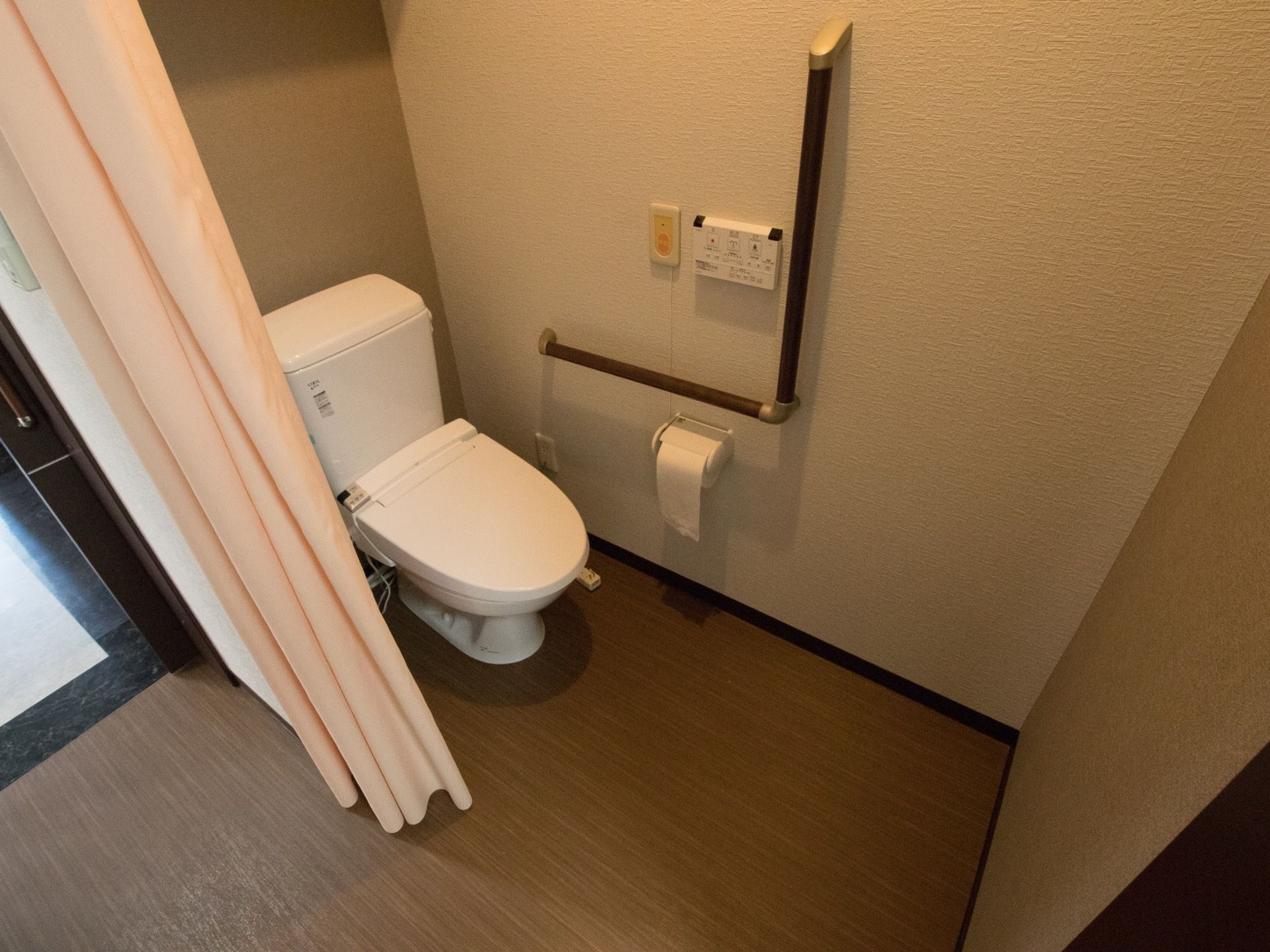 トイレにはＬ字型の手すりやナースコールが取り付けてある。扉はなくカーテンで仕切られており、閉じ込めなどのリスクはない。