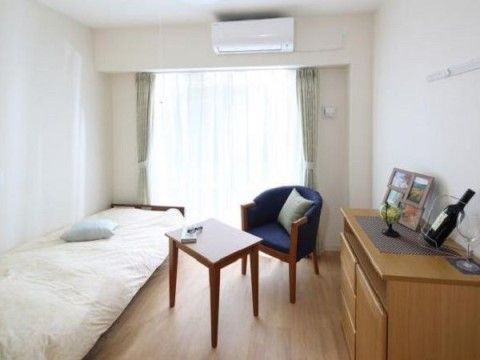 フローリングの居室にはベッドが１台、一人がけのソファーとテーブル、チェストがある。入居者様がゆったりと安心して過ごせるようになっている。