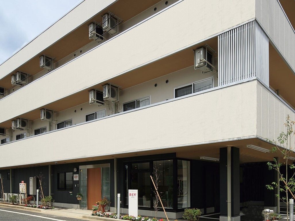 道路に面した場所にある３階建ての建物は、白と黒を基調としていて都会的である。玄関はウッド調で、建物のアクセントになっている。