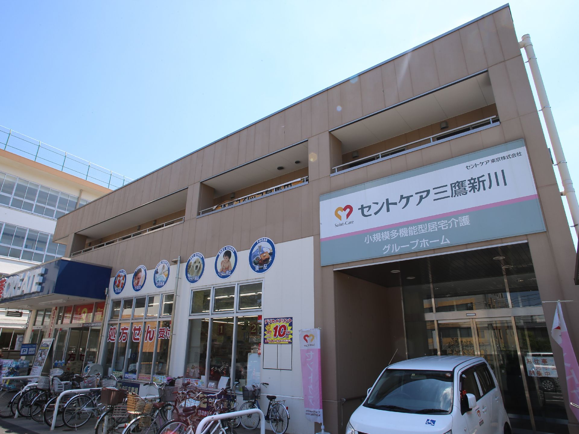 施設の外観。エントランス前に国際シンボルマークを付けた乗用車が停車している。一階にはドラッグストアが併設している。