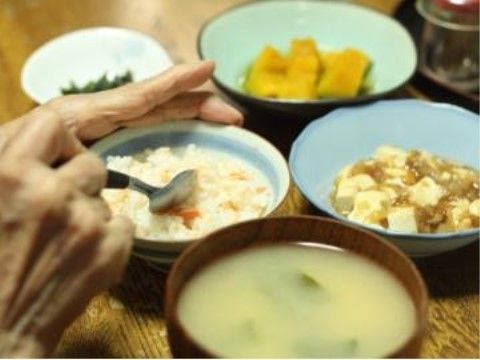 炊き込みご飯と味噌汁の他に、かぼちゃの煮物と麻婆豆腐が用意されている。入居者様がスプーンで食事をしようとしている。