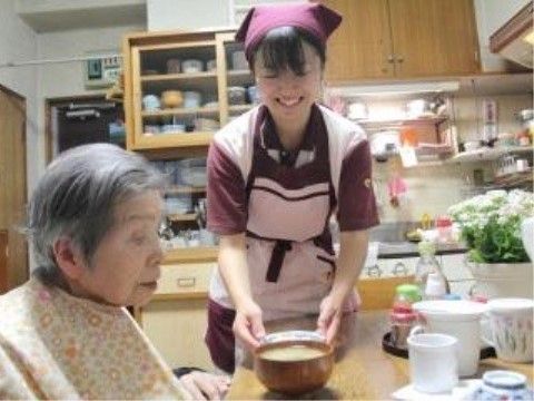 紅色の三角巾をしたスタッフに食事を配膳されている入居者様