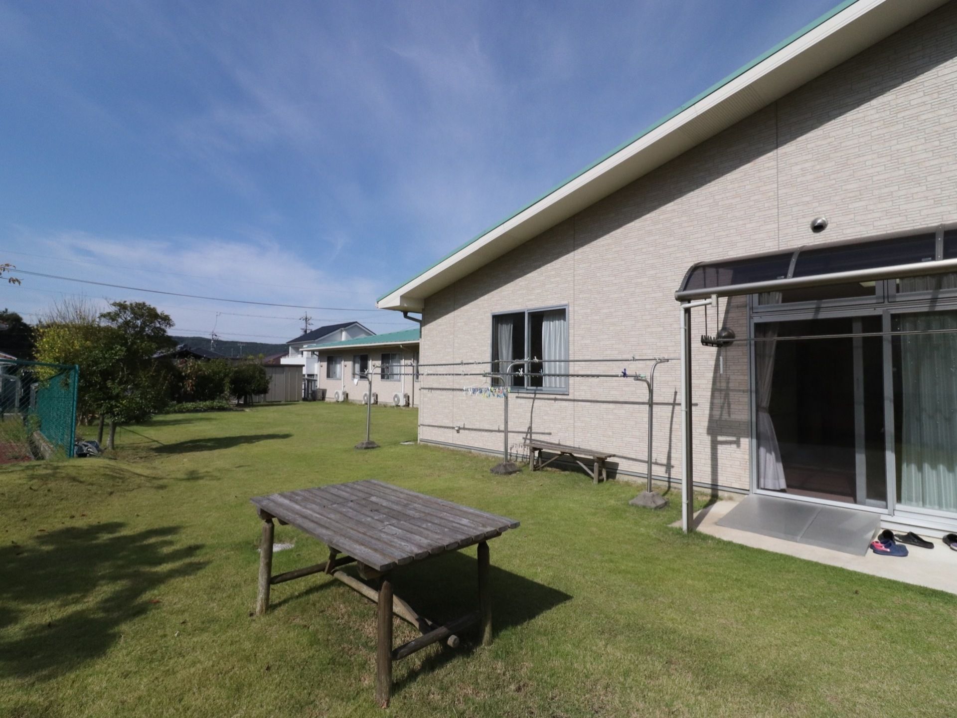 切妻屋根が特徴的な建物である。物干しざおには洗濯ばさみがいくつかはさんである。室外機が複数設置されている。