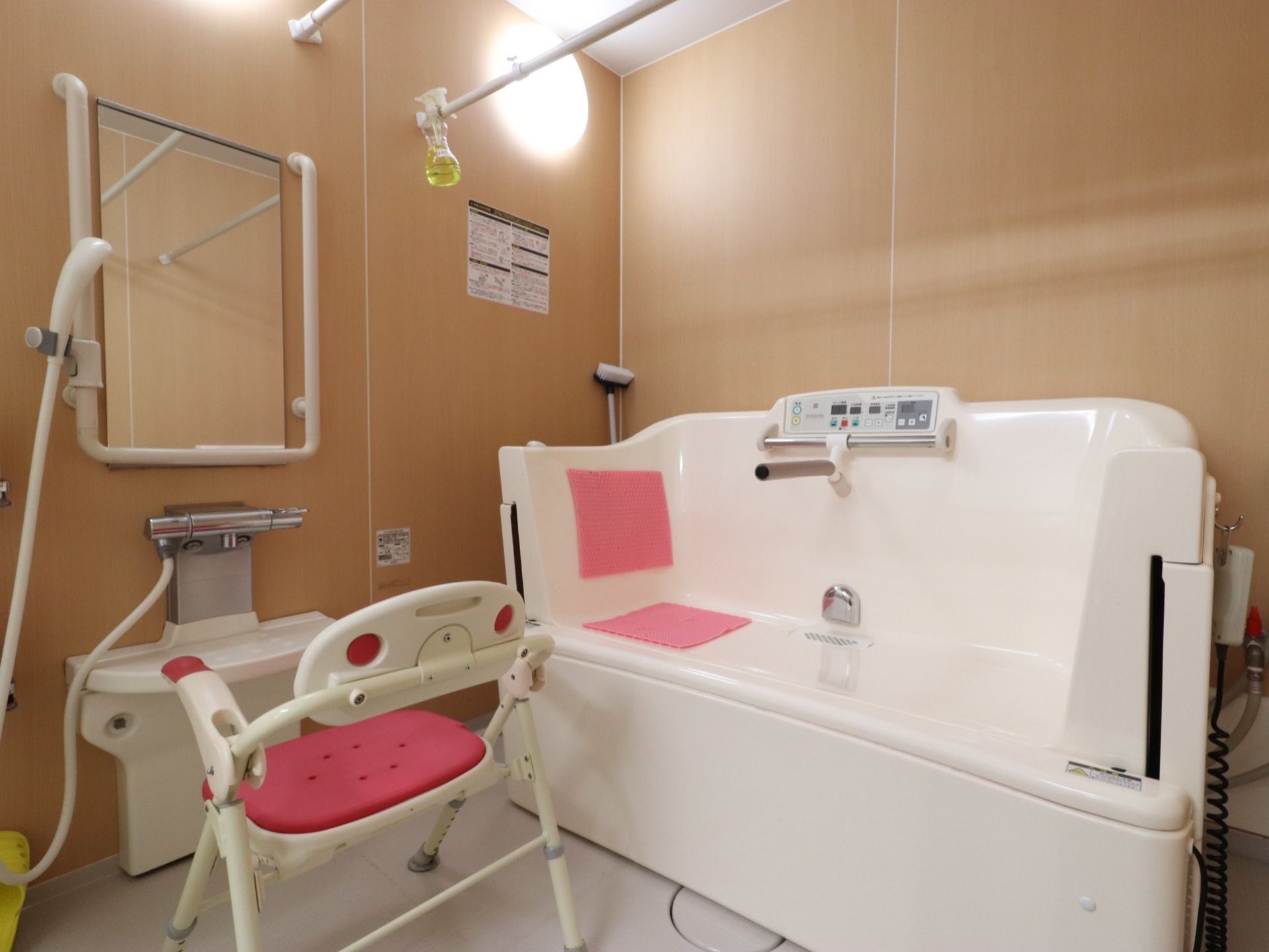 壁面は茶色、床は白い内装の浴室である。洗い場には背もたれ付きのイスがある。入浴介助用の機器が設置されている。