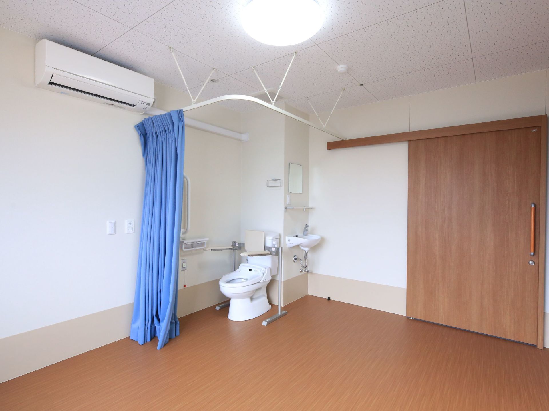 トイレ付タイプの居室である。エアコンや照明、洗面台が備わっている。出入口の扉には、スライドドアが採用されている。