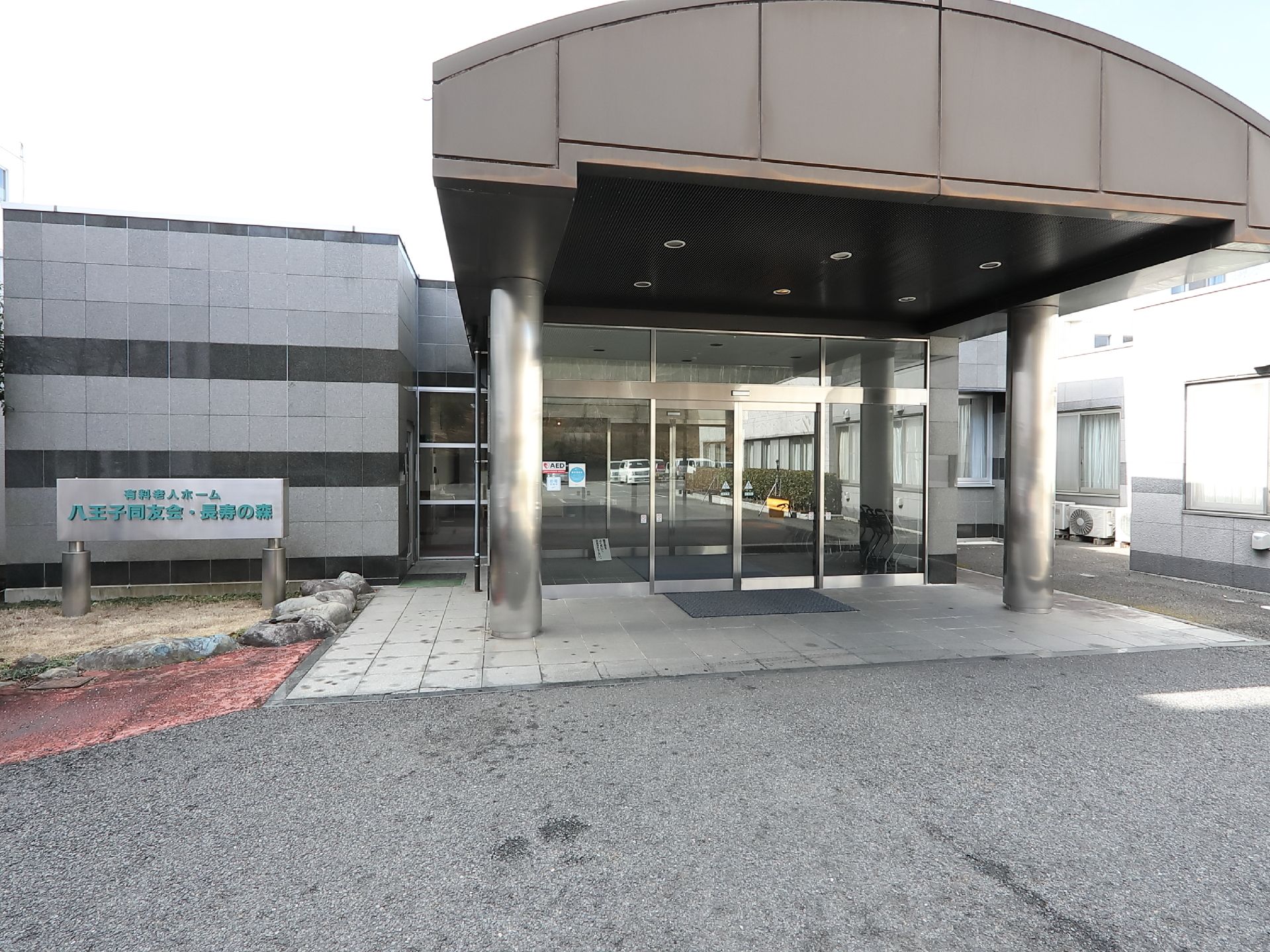 玄関前にはかまぼこ型の屋根がせり出し、車を寄せることができる。入口の左手に施設名が表示された看板が立っている。