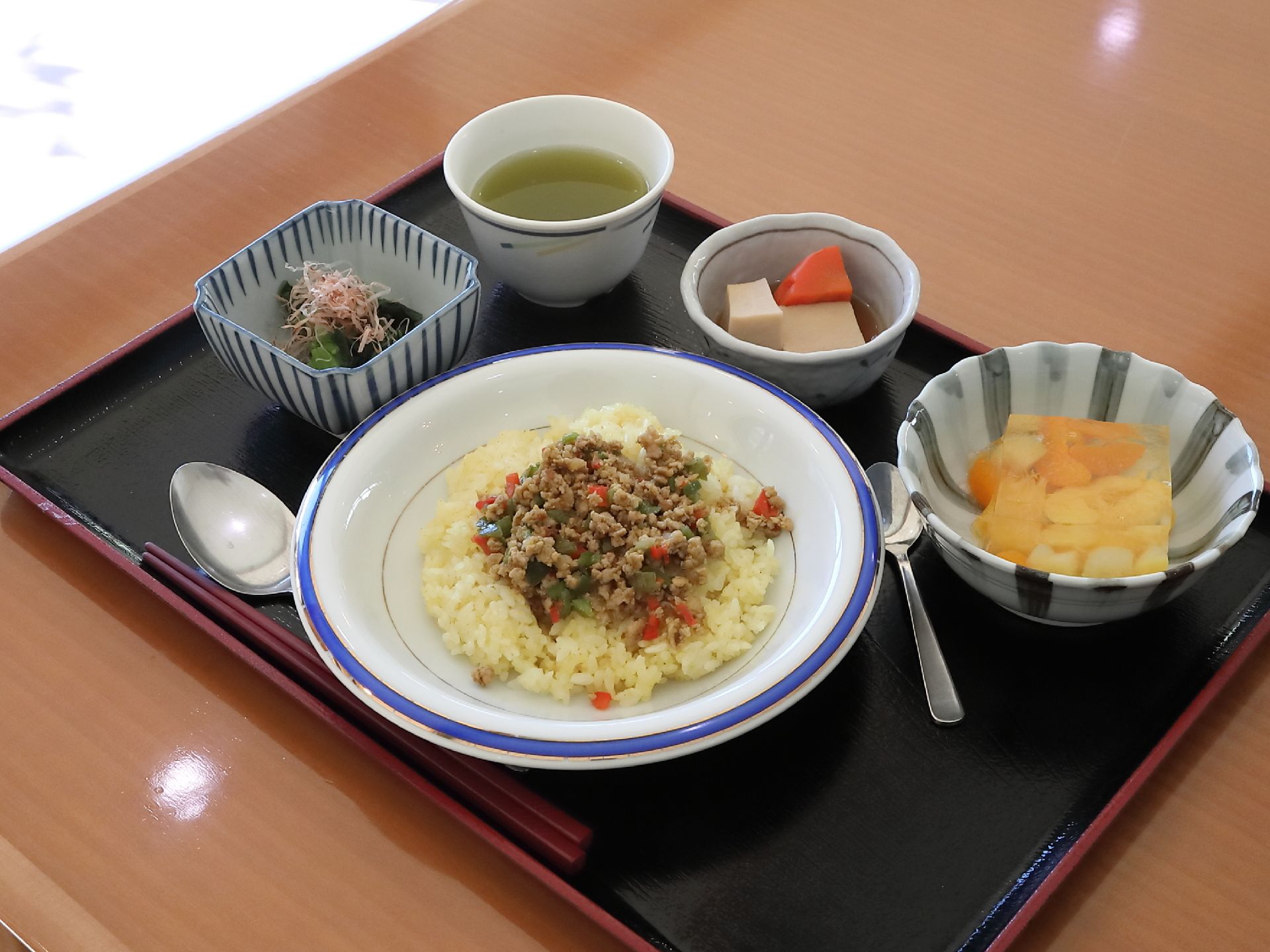 ピラフにそぼろがかかったご飯がメインで出た日のメニューの一例である。高野豆腐と野菜の煮物の小鉢やフルーツゼリーがある。