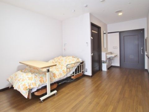 黄色い花柄の布団が敷かれたテーブル付きの介護ベッドがある居室
