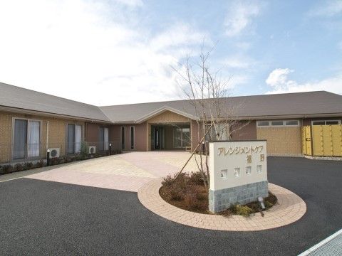 円形の植え込みに、施設名が表示された低い壁のある玄関前