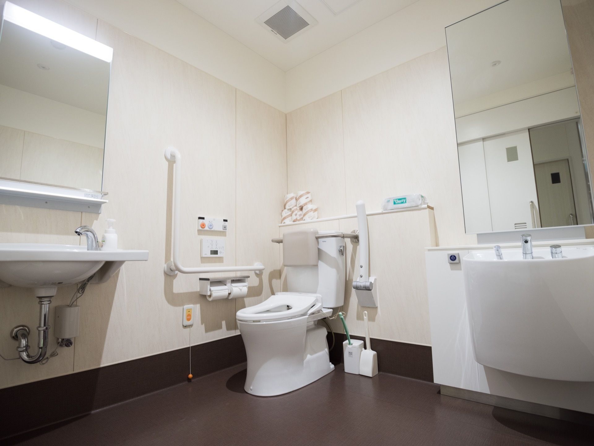 広々とした清潔感のあるトイレ空間。洋式便器とオストメイト専用トイレが設置されており、左手前に手洗器と鏡がある。