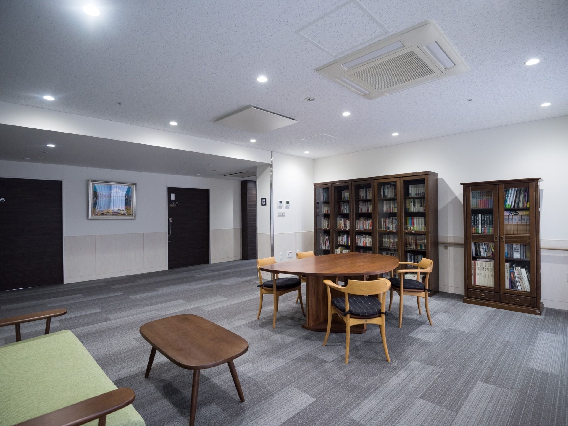 グレーの絨毯が敷き詰められた通路の一角が広くなっており、テーブルや椅子が設置されている。壁際には背の高い本棚が置いてある。