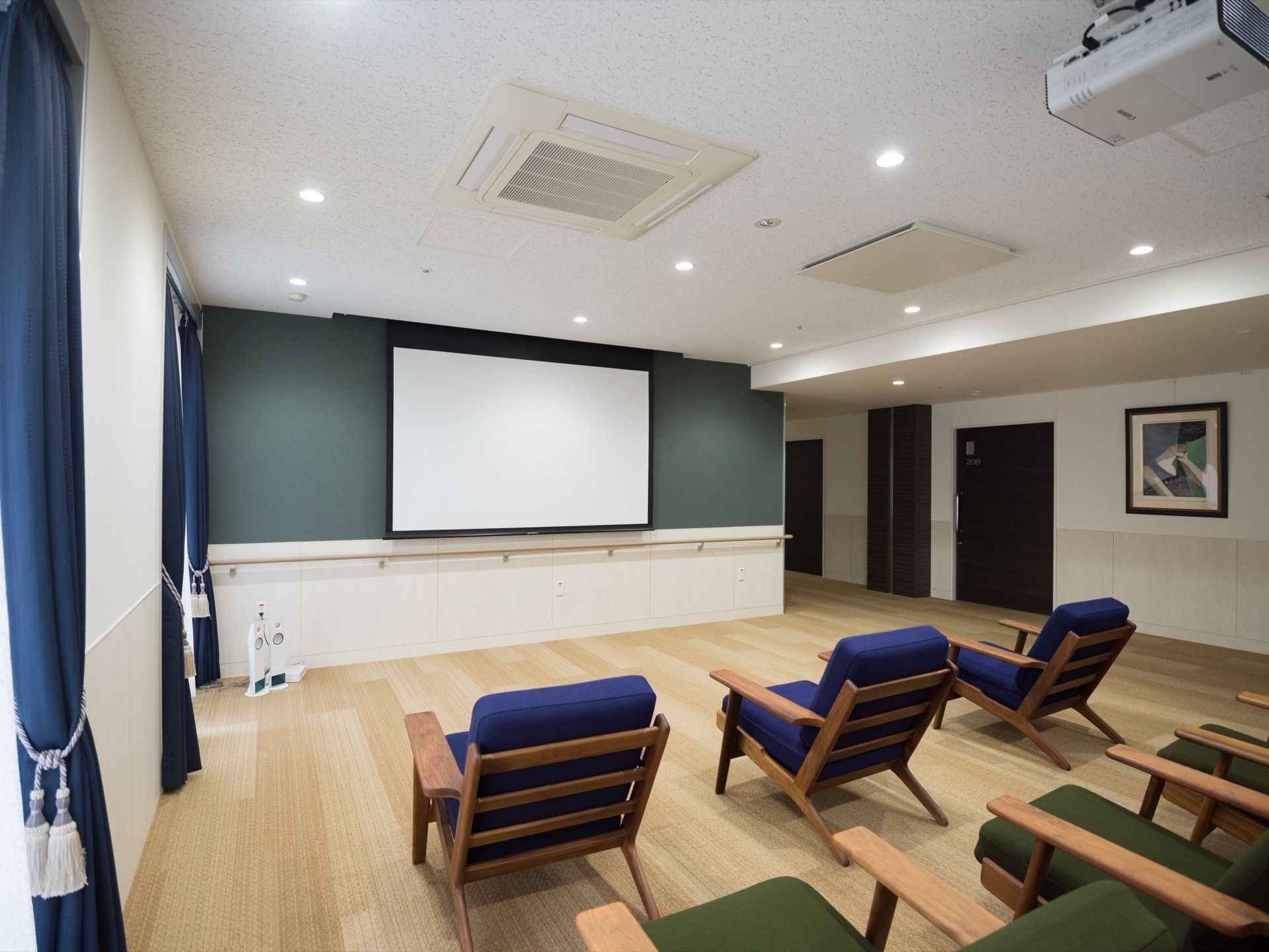 緑色と青色を基調とした爽やかな空間。緑色の壁面に大型スクリーンが設置されており、それを見やすい位置に複数の椅子が並べられている。