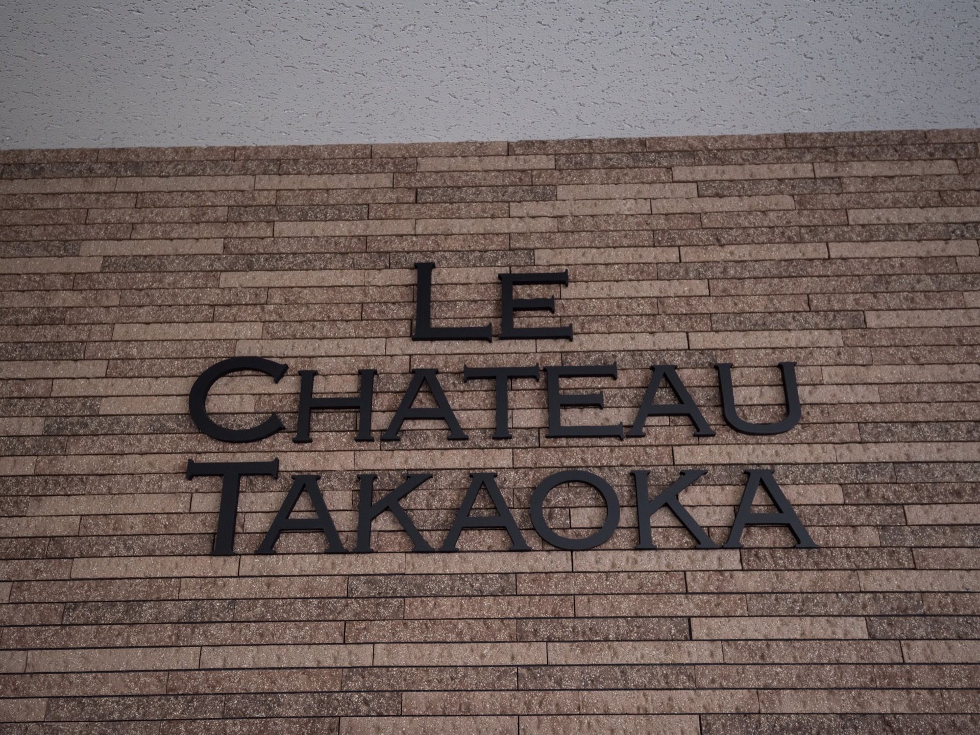 石造り調の壁面に、施設名がフランス語で浮き彫りに記されている。黒いアイアン調の質感と書体が、西洋風の印象を与える。