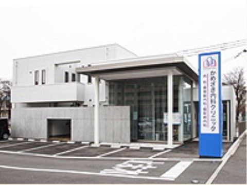道路に面した新しい２階建の建物。敷地は舗装されており、駐車場スペースがある。２階のベランダが玄関のひさしを兼ねている。