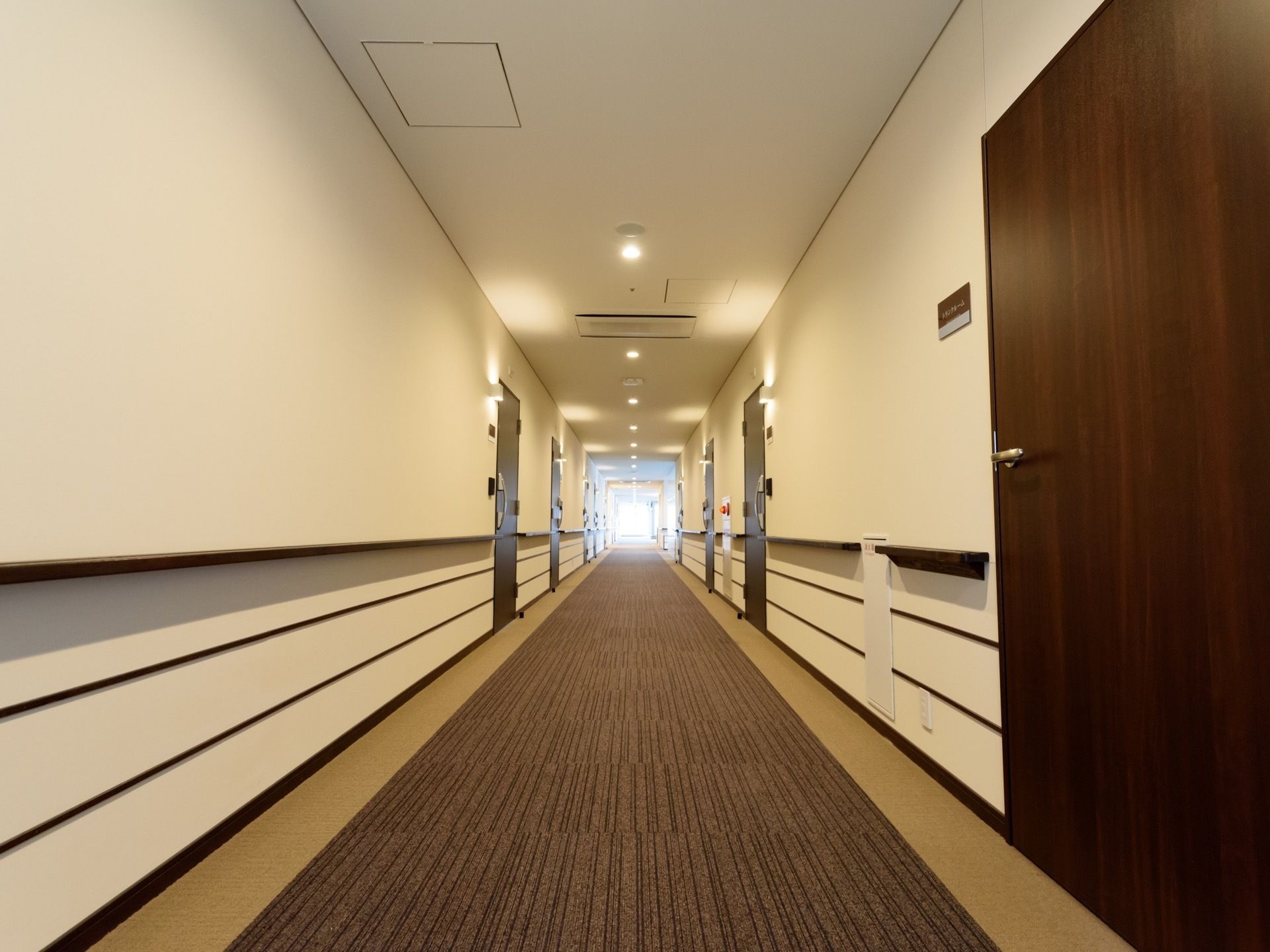 通路の壁面には手すりが設けられており、幅にゆとりをもたせている。天井や居室の入口にある照明の光が、空間に変化をつけている。
