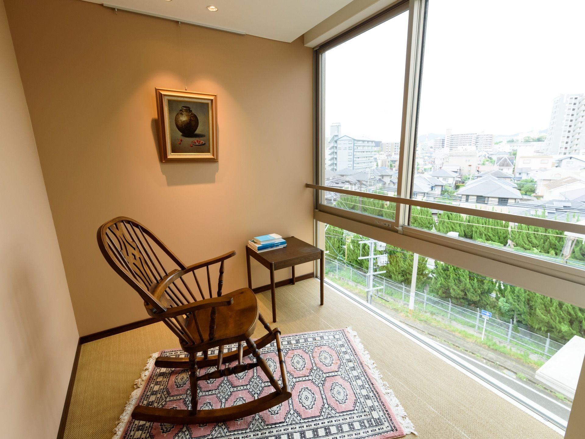 小さな小部屋から外の景色を眺められるタイプのバルコニーである。マットの上にロッキングチェアがあり、壁側に小さなテーブルが置かれている。