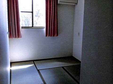 清潔感のある白い壁の和室である。窓には網戸が入っており、窓の向こうには木が見える。窓から差し込む光が明るい。