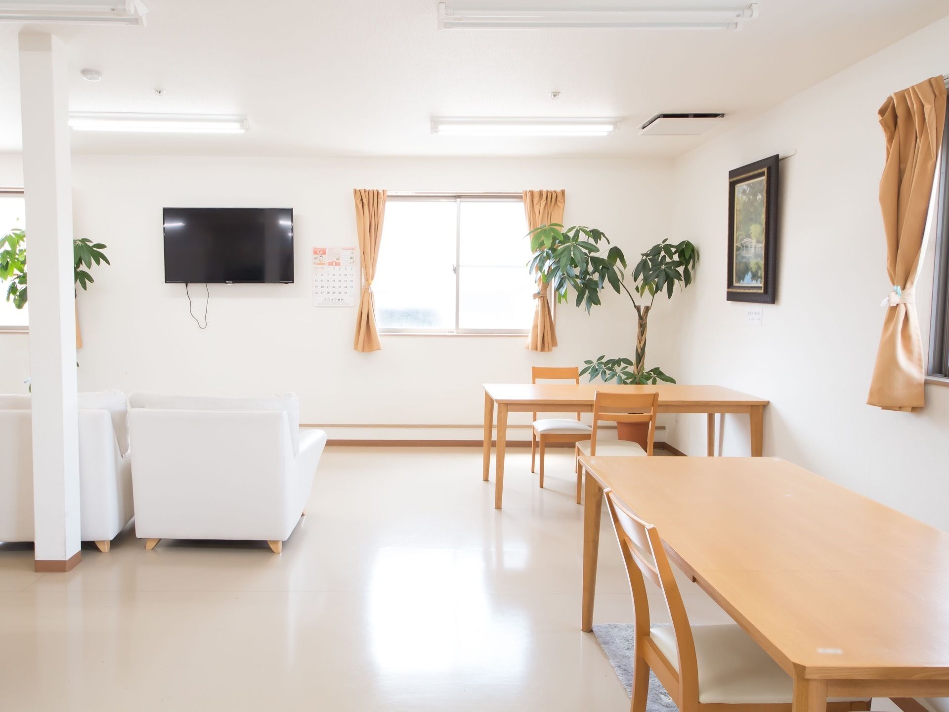 ダイニングテーブルやソファがゆったりと配置されている。ソファの前の壁にテレビとカレンダーが架けられている。