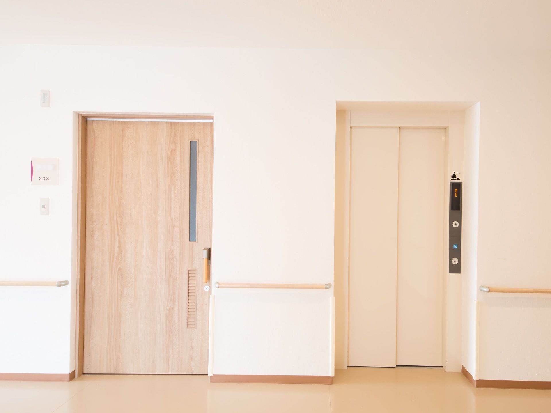 廊下の壁に手すりが備わっており、エレベーターと居室のドアが並んでいる。居室のドアの横に部屋番号の書かれたプレートがついている。