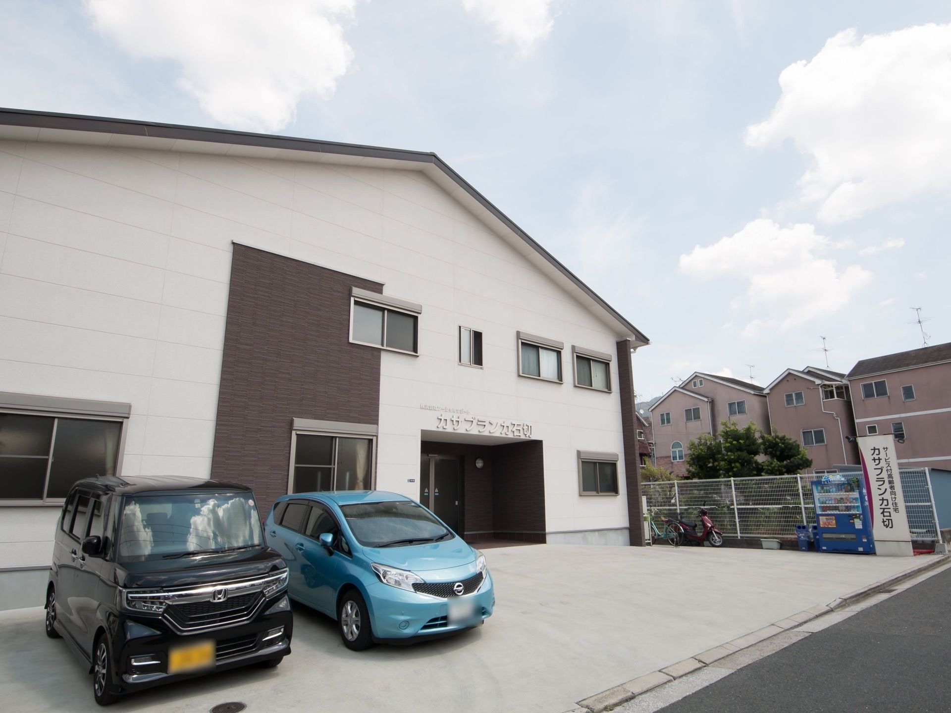 切り妻屋根の二階建ての建物で、正面に駐車スペースが整備されている。施設名の書かれた看板の横に、自動販売機がある。