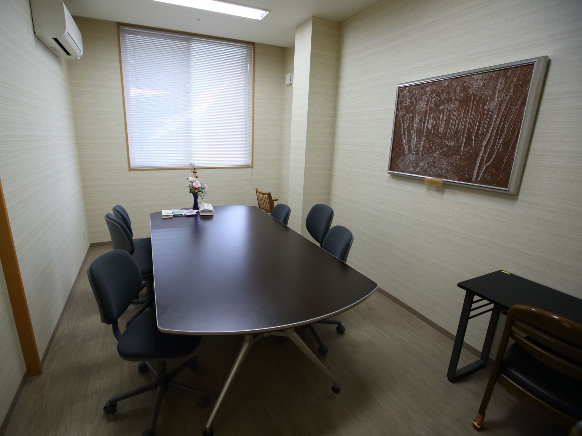 談話室に黒のテーブルと椅子が６脚置かれている。白の壁には絵画が飾られており、エアコンが設置されている。