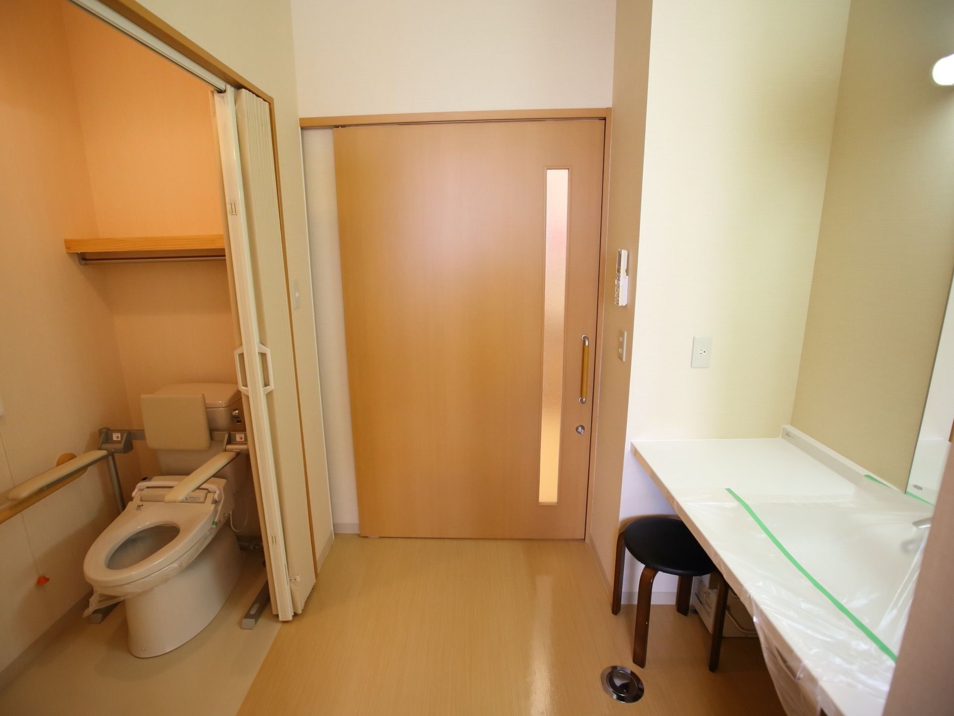 トイレのドアは木目調でスライド式となっている。便座には補助器具が設置されており、近くにナースコールが備わっている。