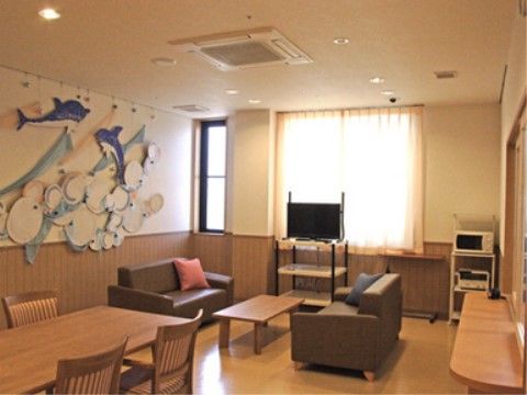 壁面には季節を感じる掲示物が飾られている。床はフローリングで段差がない。ダイニングセットと、応接セットが設置されている。