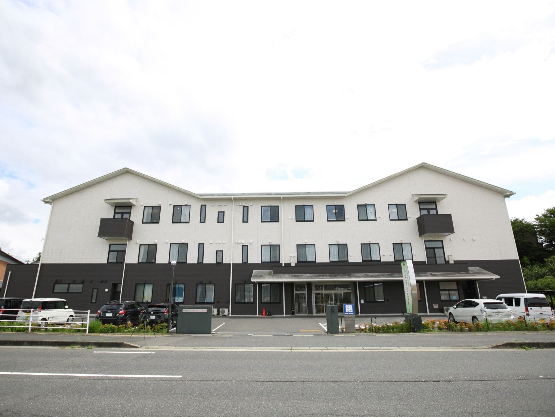 白い外壁の建物で、３階建てである。建物の両端が三角屋根になっている。施設の前には駐車スペースが広がっている。