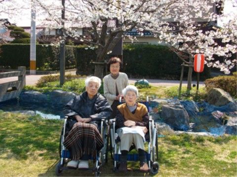 満開の桜の木の下でこちらを向いて微笑んでいる入居者様