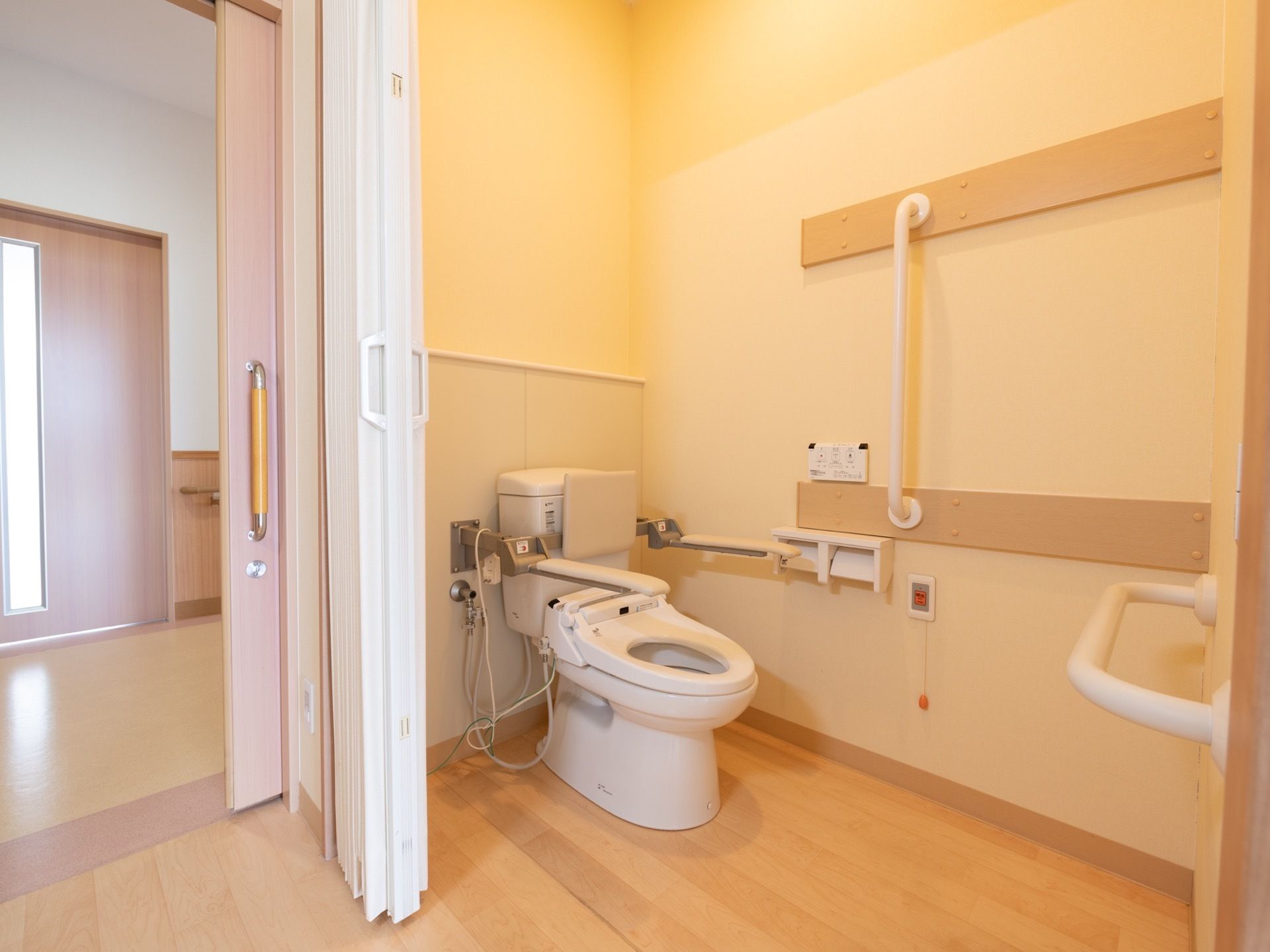 居室の一角に、仕切りに囲われたトイレがある。壁には手すりやつかまり用の棒が取りつけられているほか、ナースコールも付随している。