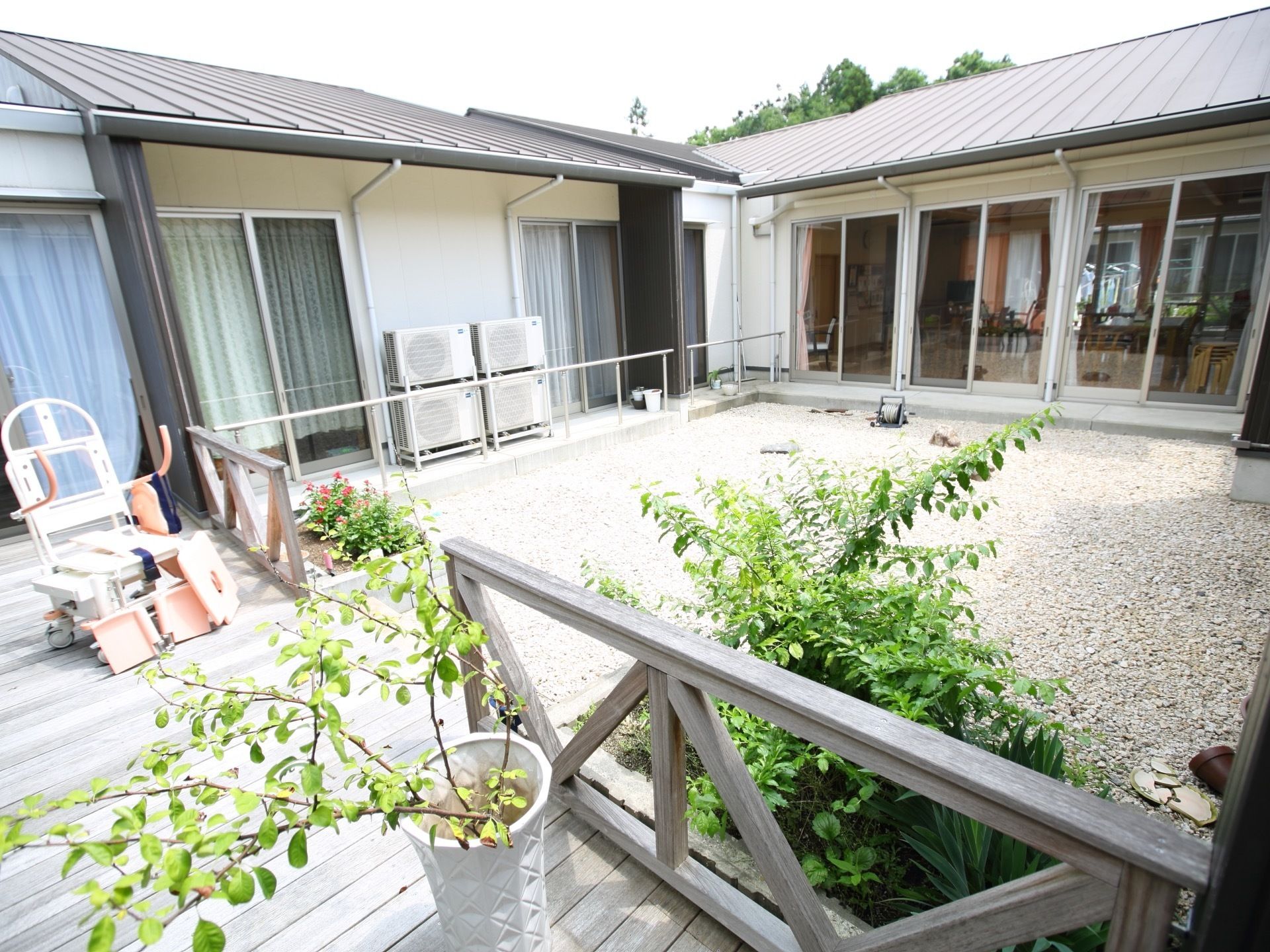 庭の左側にウッドデッキがあり、鉢に植えられた植物が置かれている。庭とウッドデッキの間には木製のフェンスが設置されている。
