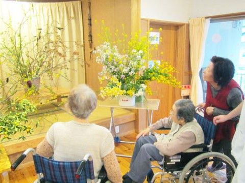 車椅子に乗った入居者様と一緒に飾られた花を眺めるスタッフ