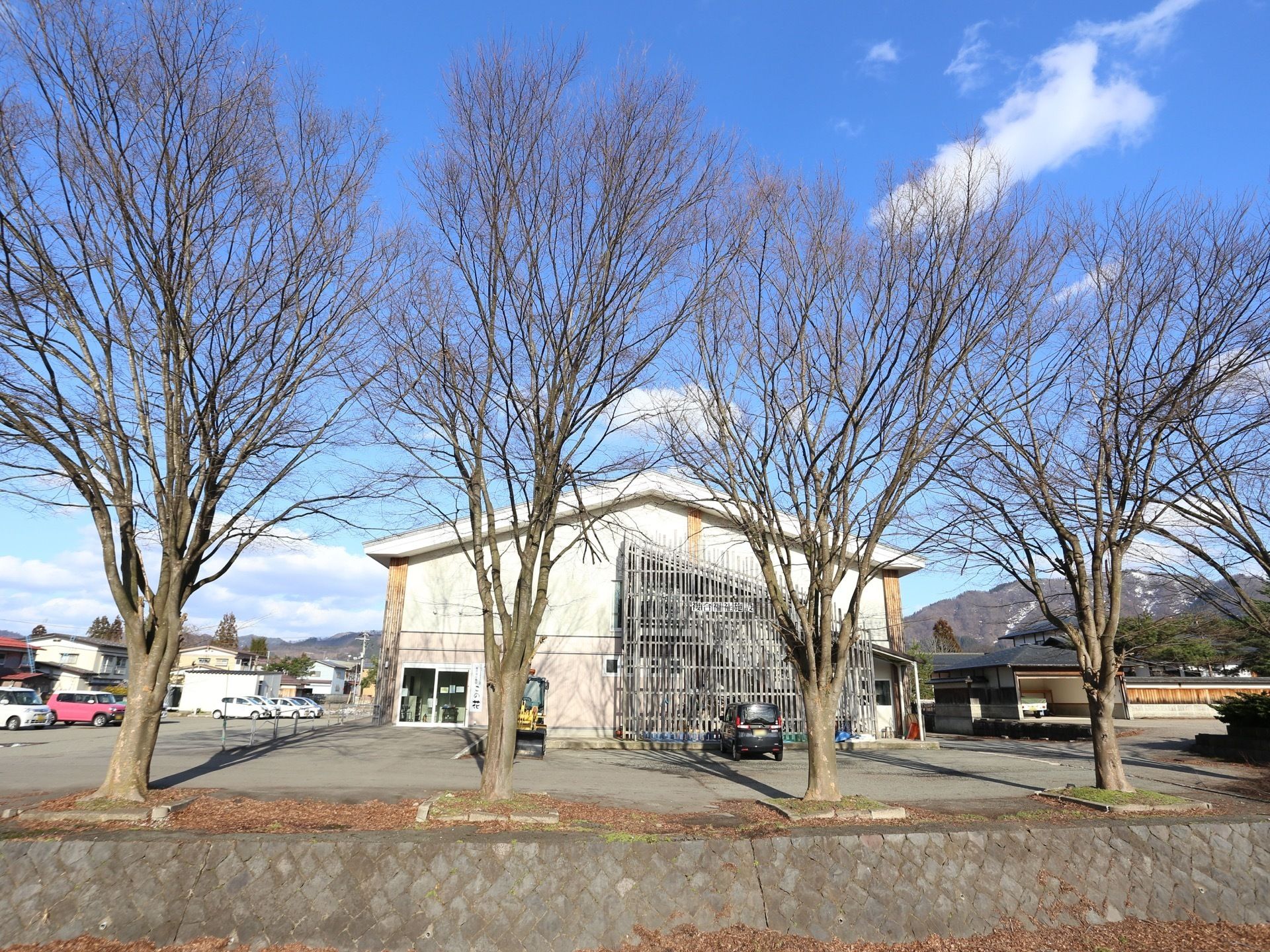 晴天の日に木立の奥に立地している2階建ての施設である。駐車場を完備しており、２台の乗用車が停車している。