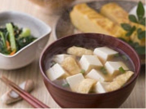 とうふと油揚げの味噌汁の奥に卵焼きと小鉢が並ぶ食事