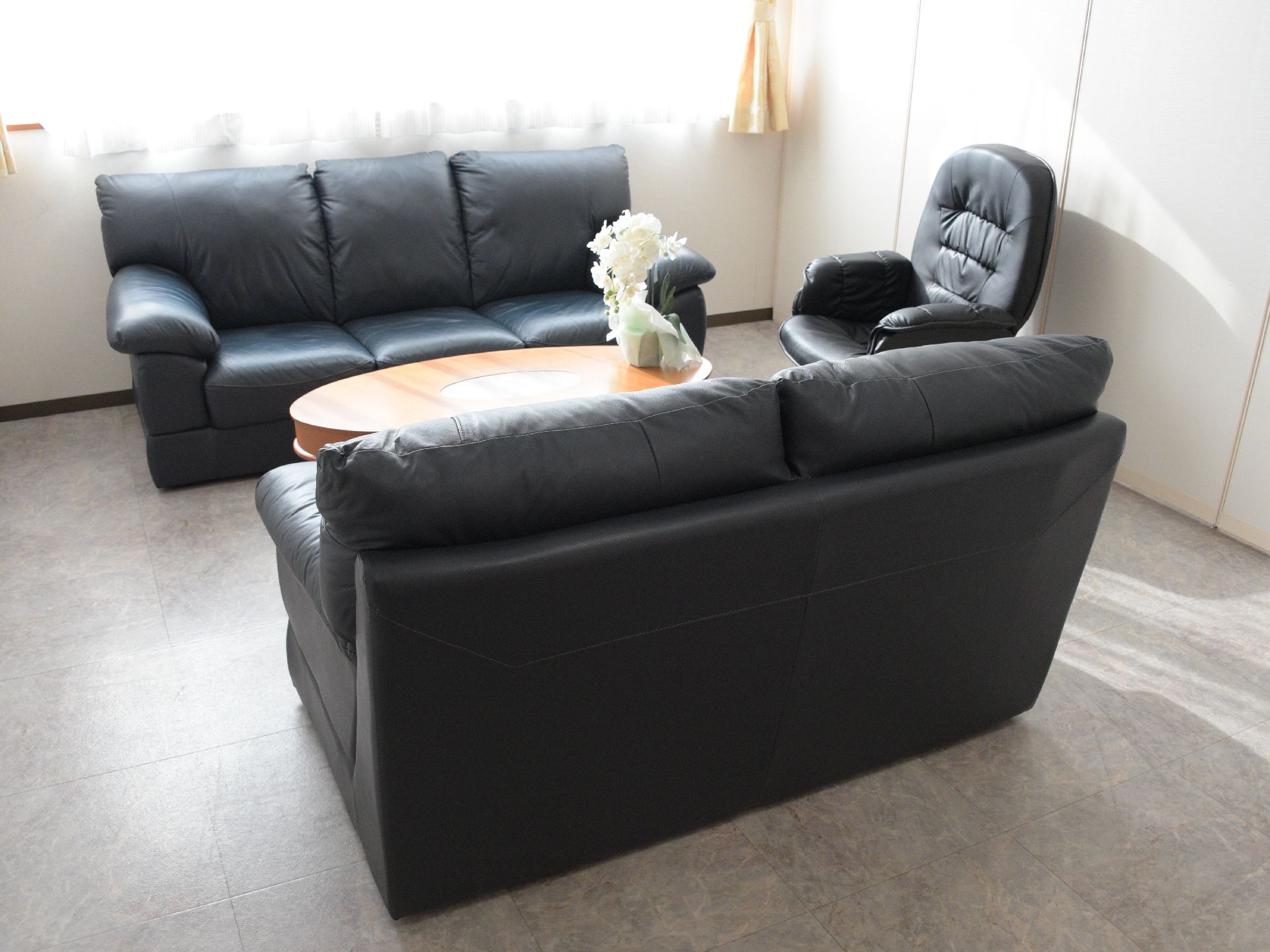 黒くゆったりとしたソファーのある部屋。日当たりもよく、ローテーブルには花もいけられているので、リラックスして過ごすことができる。