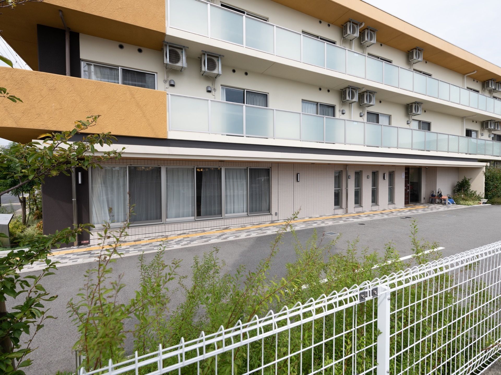 壁は白とオレンジに塗り分けられている。各居室にはベランダがある。施設周囲にはフェンスに沿って植栽が植えられている。