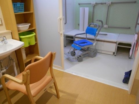 脱衣所の洗面台の前には椅子がある。棚にはカゴが置かれている。浴室内には手すりと介護用シャワーチェアが用意されている。
