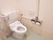洗練された壁紙が貼られた、清潔感のあるトイレの様子。温水洗浄便座に背もたれパッド、しっかりしたL字型の手すり、呼出ボタンが設けられている。