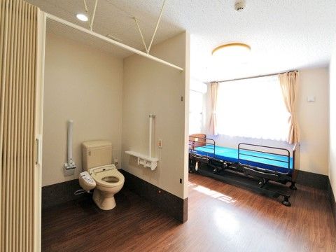 居室には窓があり、窓際には柵付きのベッドが置かれている。トイレもあり、扉の代わりに開け閉めしやすいカーテンが取り付けられている。