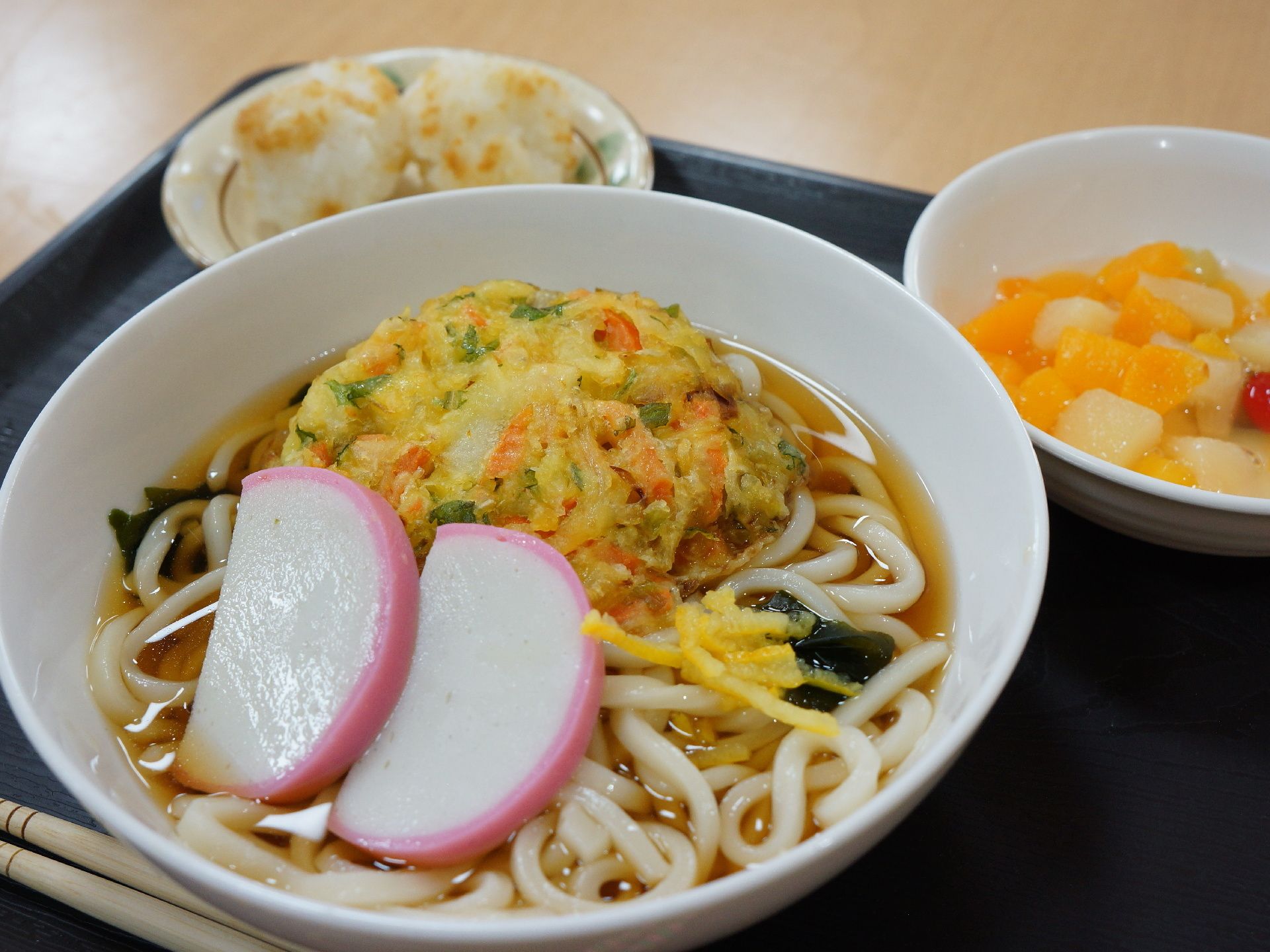 メインメニューのうどんにはワカメが入っていて、野菜かき揚げが添えられ、カロリーと栄養バランスも考えられている。