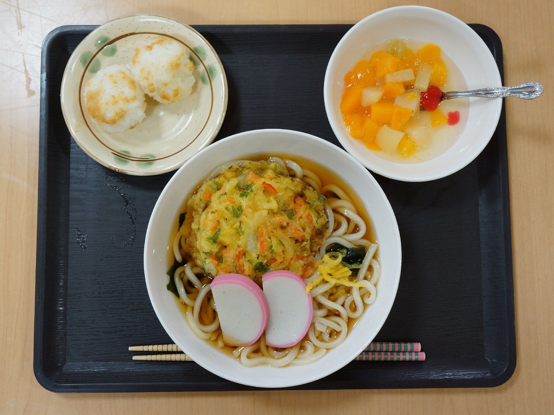 ある日の食事、メニューはかき揚げとかまぼこの乗ったうどんと味噌おにぎが二つ、デザートにフルーツポンチ。