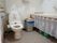 洋式トイレで、壁に手すりがついているので、立ち居を助けてくれる。レースで一部隠されたところに掃除用具などが置いてある。