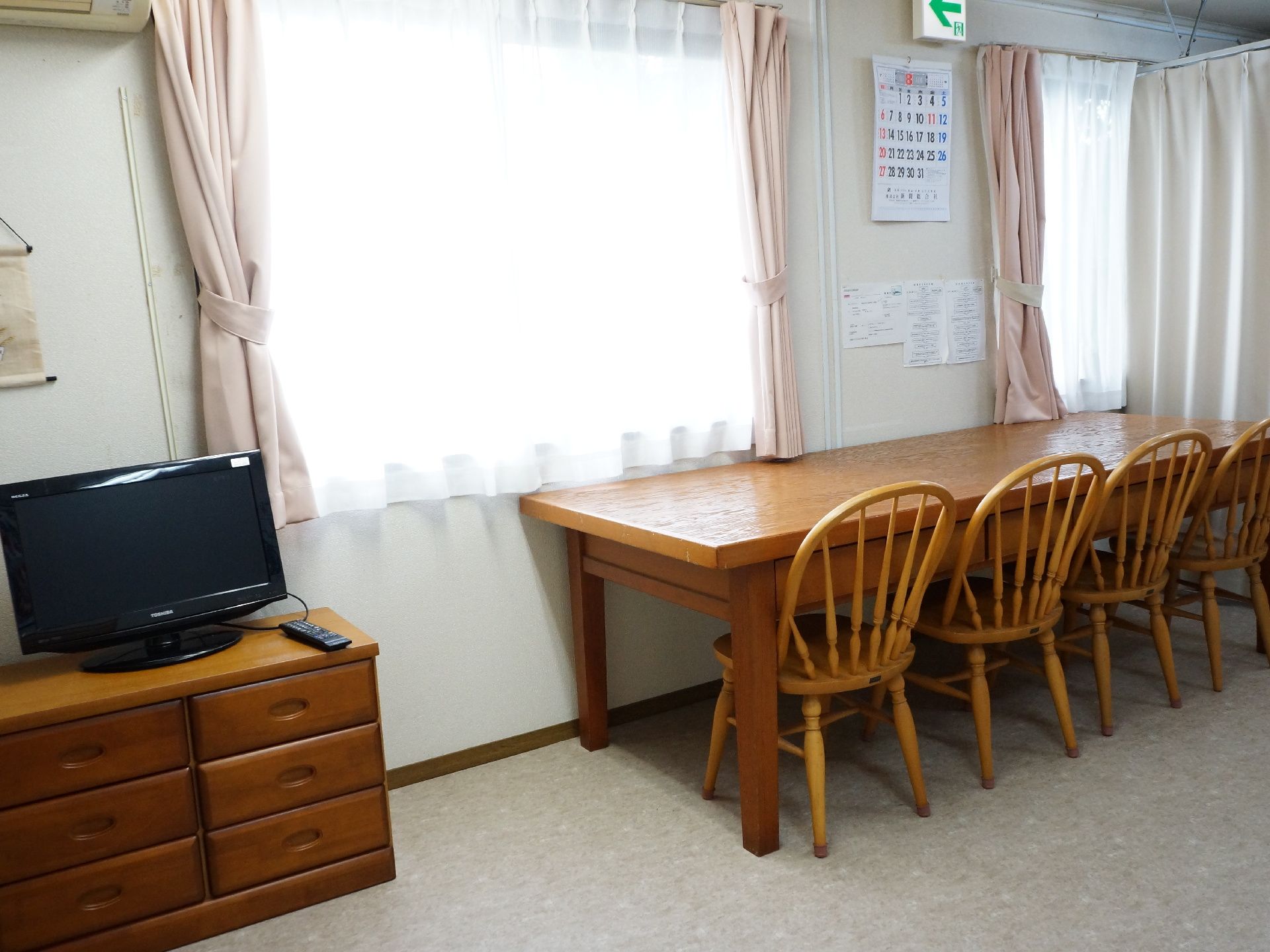 エアコンが完備の部屋で、カーテンで仕切られている。チェストの上に、テレビが設置してある。木製テーブルが一台あり、椅子が三つセットしてある。