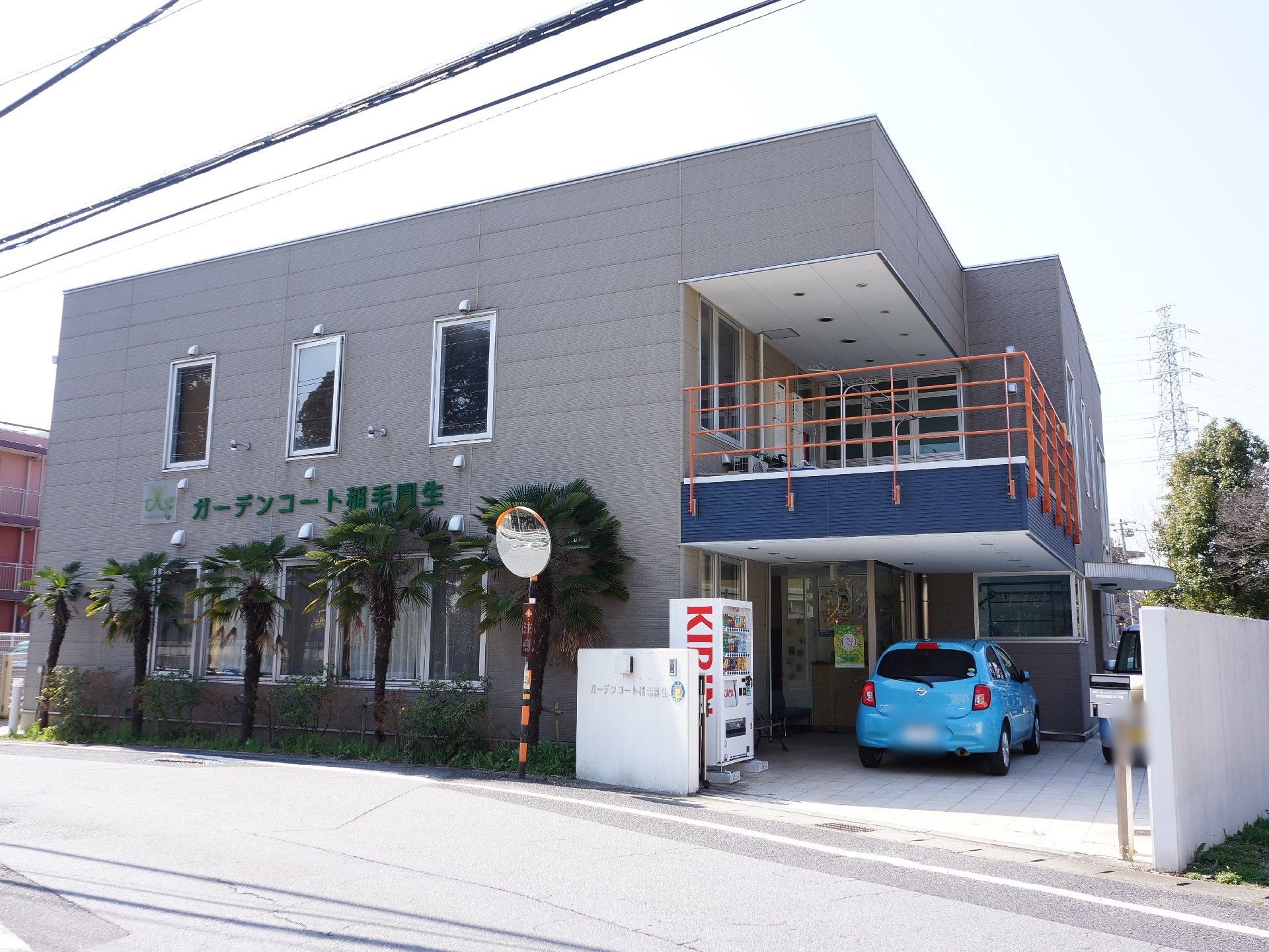 施設外観。グレーの壁でまわりに植木がある。