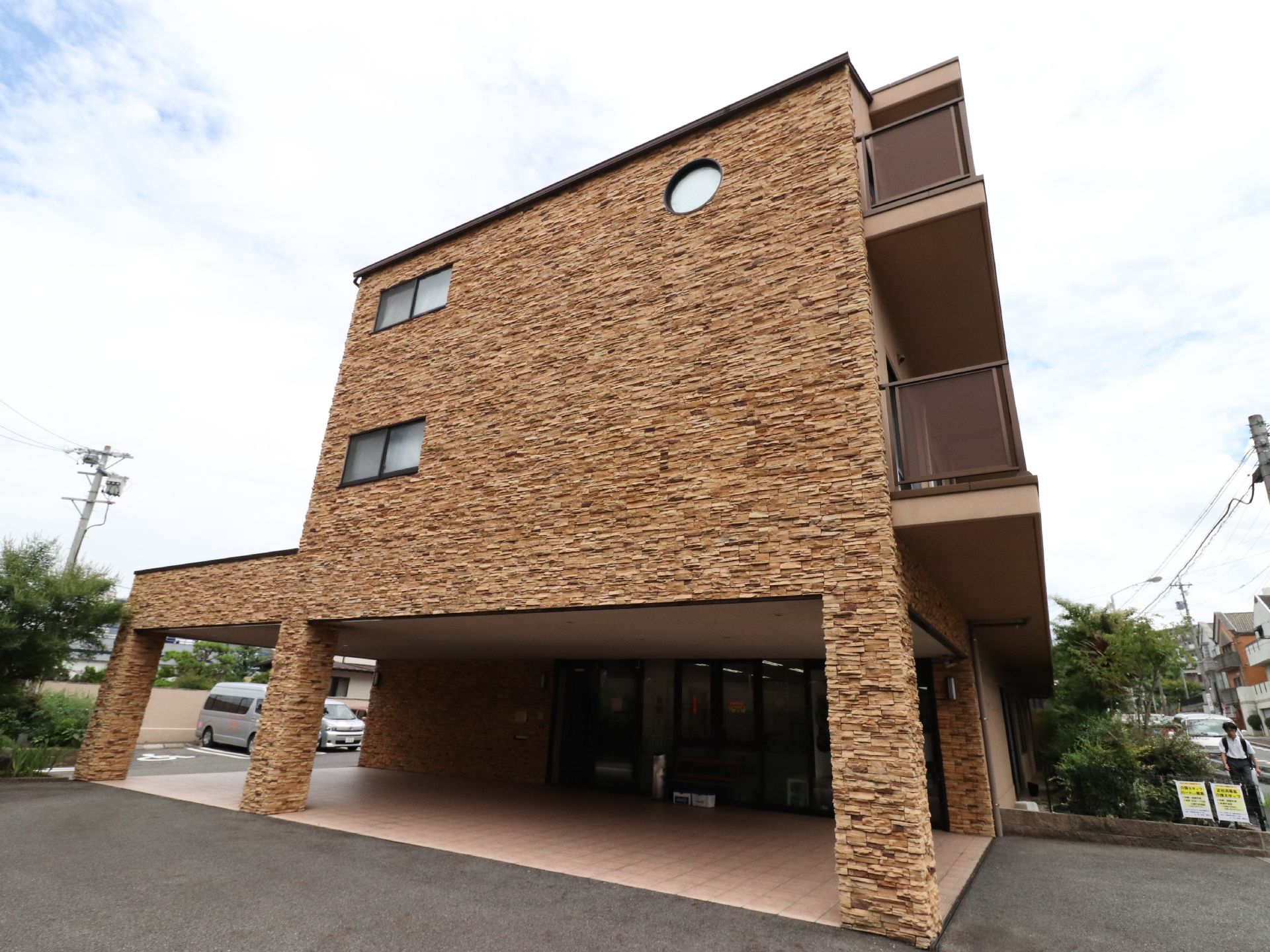 正面から見た施設は壁に凹凸があり、より立体的に見せている。周囲には綺麗に剪定された木々が植えられている。