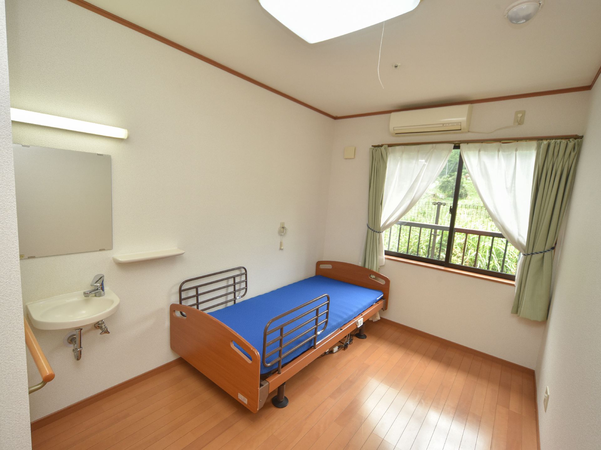 居室は窓があり、明るい自然の光が降り注ぐ。エアコンに手洗い場、ベッドを部屋に完備している。床はフローリングで段差はない。