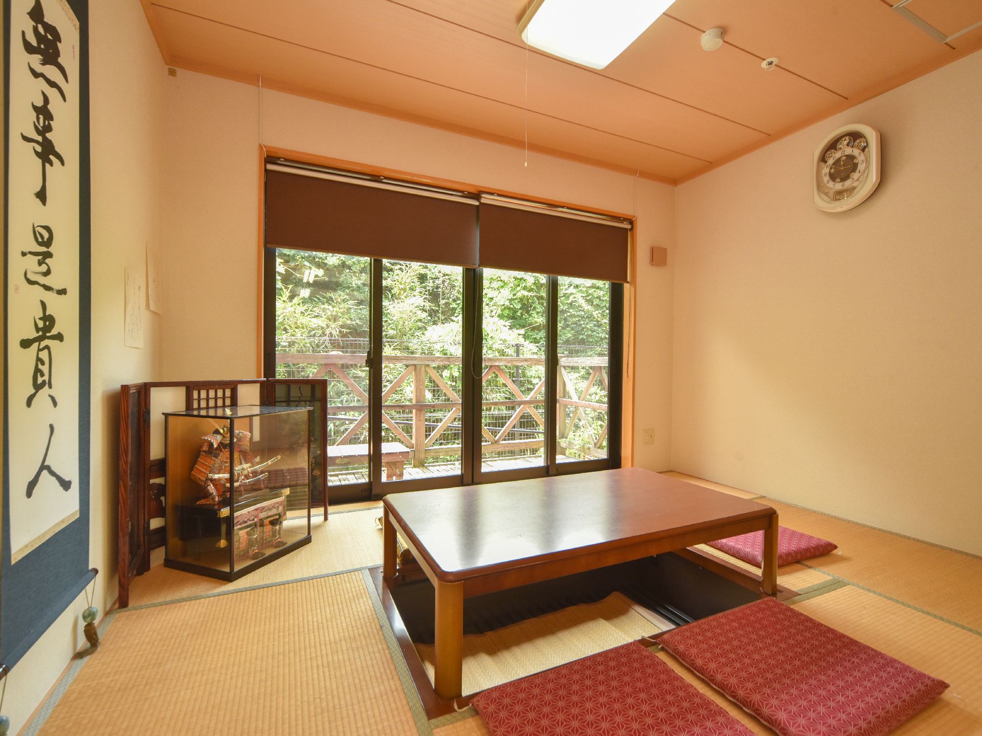 和室は掘りごたつタイプで利用しやすい。日本人形に掛け軸が飾られている。窓の外は緑あふれる景色が広がっている。