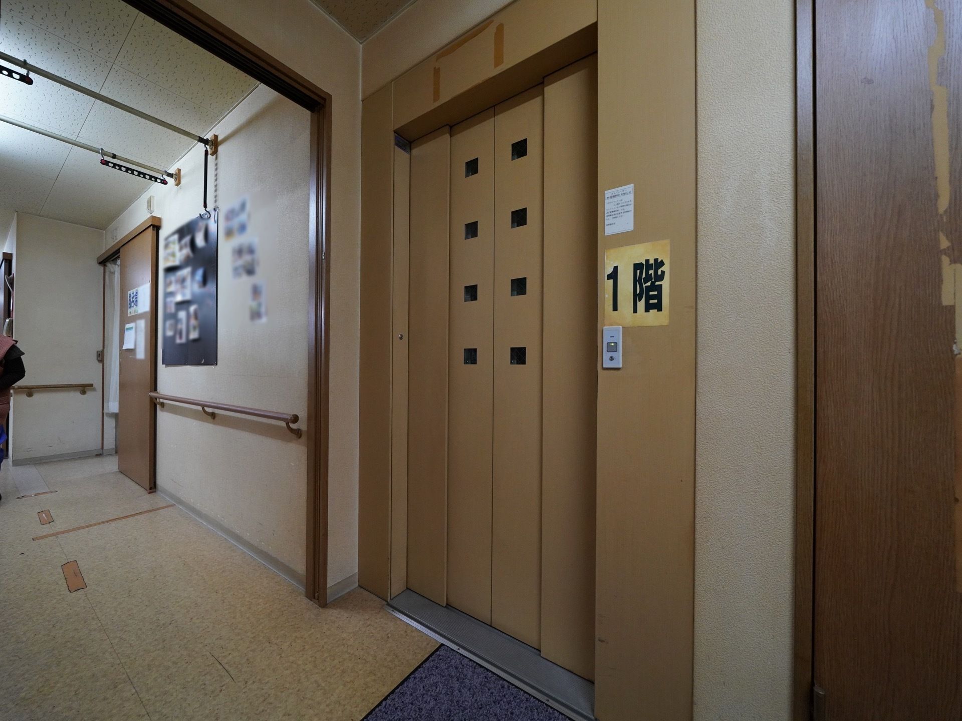 ドアがベージュ色のエレベーターが１基設置されている。ドアの横には大きく１階と書かれた黄色い紙が貼られている。